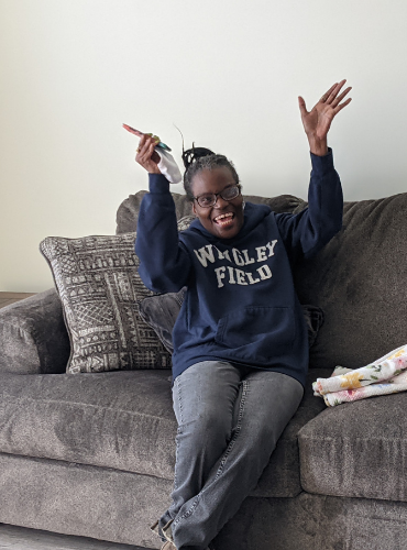 Black woman joyfully raises hands on her couch at her home