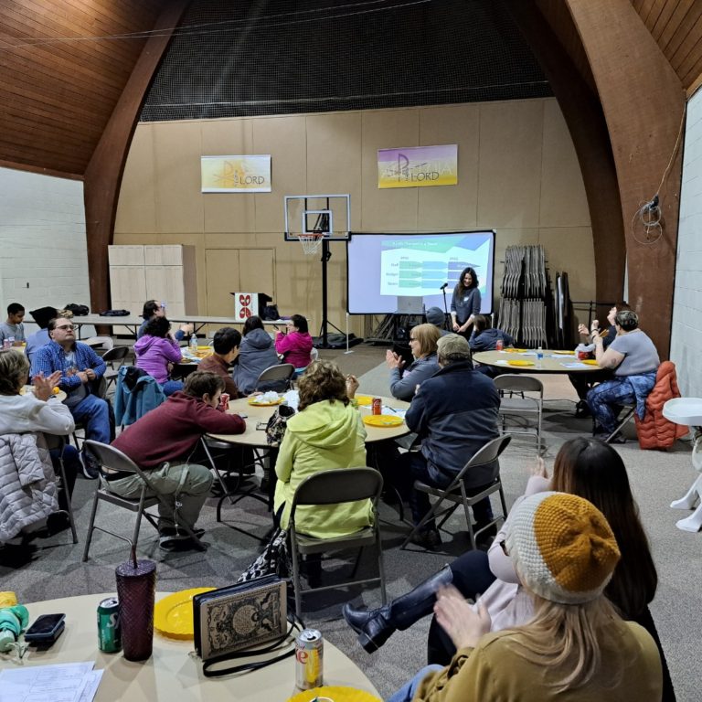 People sit at tables in a large room for co-op meeting