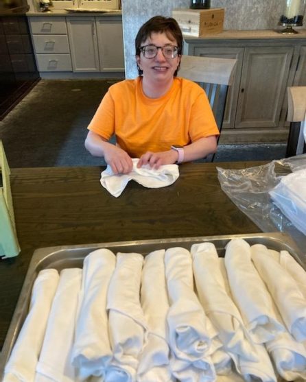 White woman in orange shirt at work rolling silverware