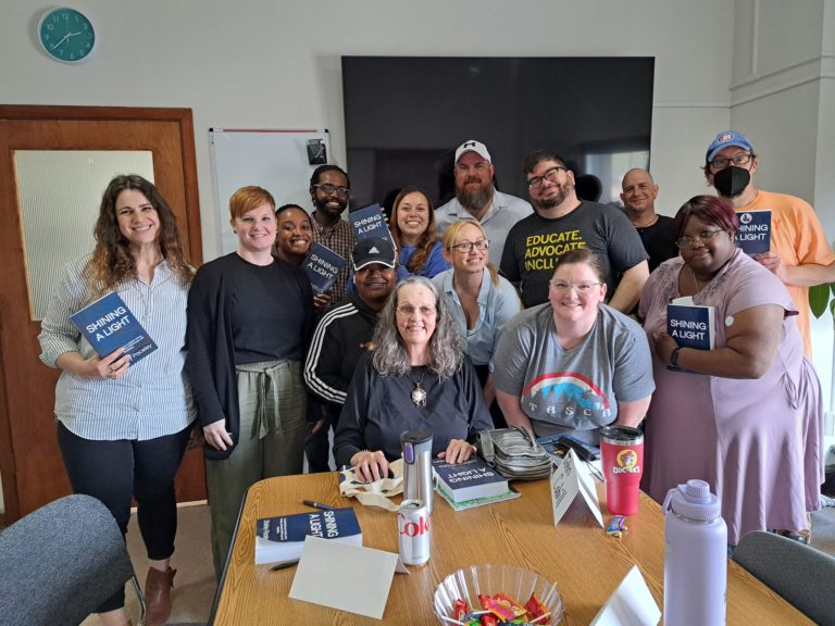 CC staff book club hold up books while posing with book author Shirley Paceley, a white woman with grey hair.